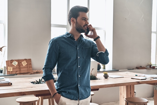 Gutes Gespräch mit dem Kunden. Hübscher junger Mann, der am Smartphone spricht und mit einem Lächeln wegschaut