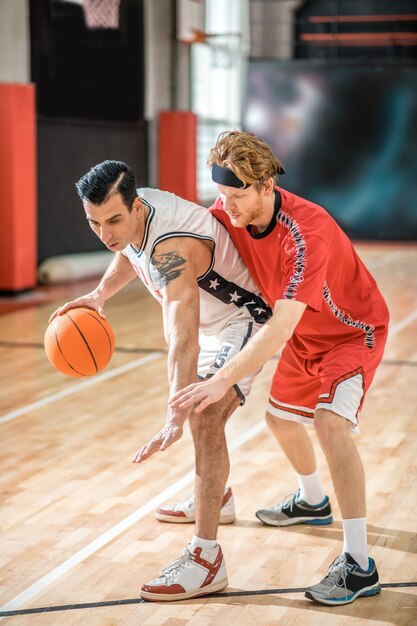 Gutes Spiel. Zwei junge Männer, die Basketball spielen und aufgeregt schauen