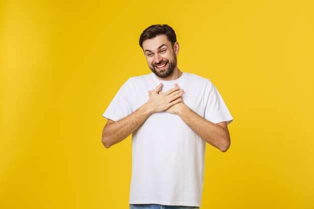 Gutherziger, fröhlicher Hipster lächelt glücklich, schließt die Augen vor Vergnügen, hält die Hände am Herzen, drückt angenehme Gefühle, Sympathie und große Liebe aus