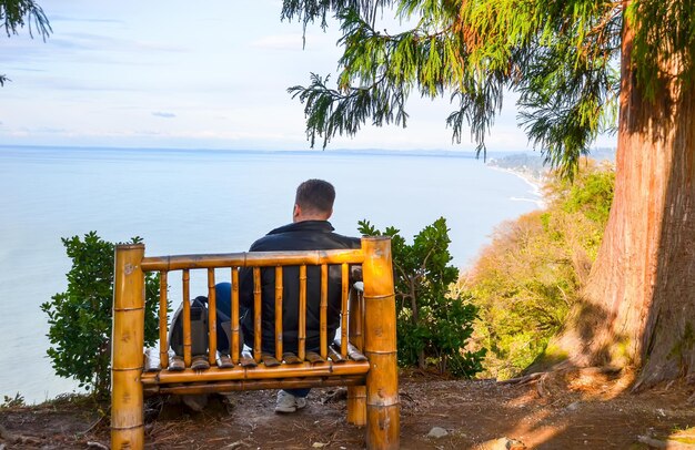 Guy disfruta de las vistas del Mar Negro en el banco del jardín botánico Georgia Batumi