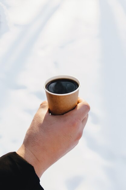 Guy hält eine Pappbecher Kaffee in der Hand im verschneiten Wald