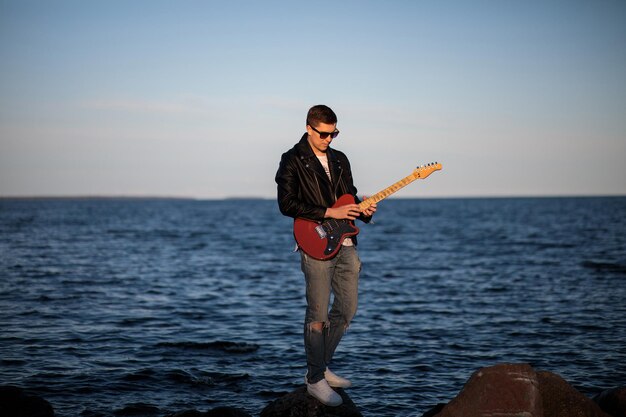 Guy in Sonnenbrille spielt die E-Gitarre auf dem Hintergrund des Sees
