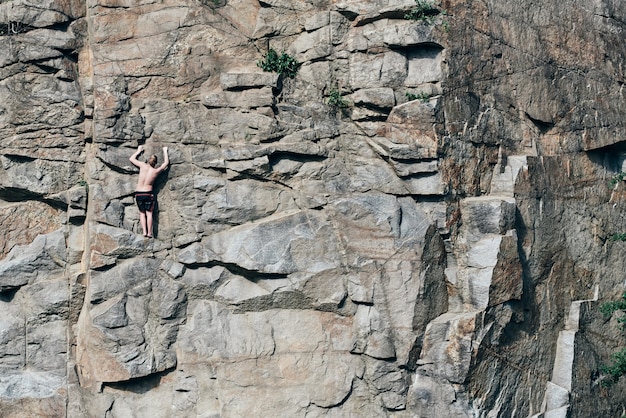 Guy klettert auf Felsen und sieht extrem aus. Haubenoberfläche, in Rissen. Felsen. Steinmauern. furchtlose Person.