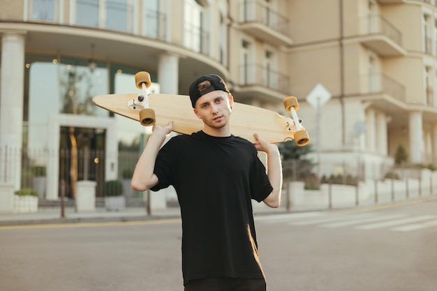 Guy Model in dunkler Kleidung posiert mit Longboard auf der Straße