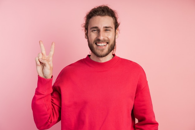 Guy mostra o sinal V, o sinal da vitória, paz. Jovem positivo.