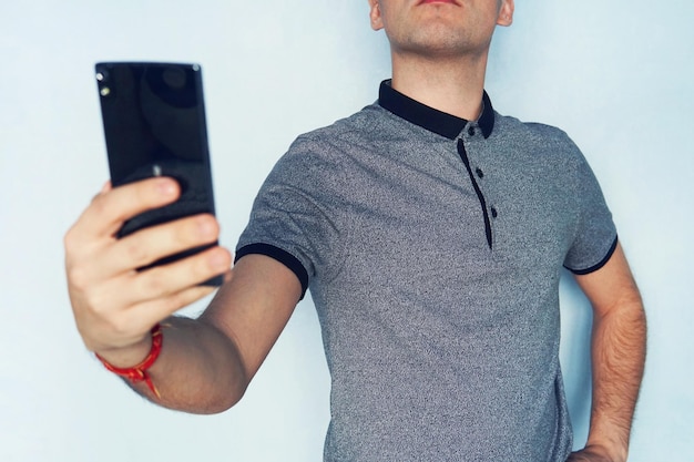 Guy nimmt sich auf einem Mobiltelefon auf Ein junger Mann macht ein Selfie Ein Mann liest SMS auf einem schwarzen Smartphone Eine Person schaut auf blauem Hintergrund in den Telefonbildschirm