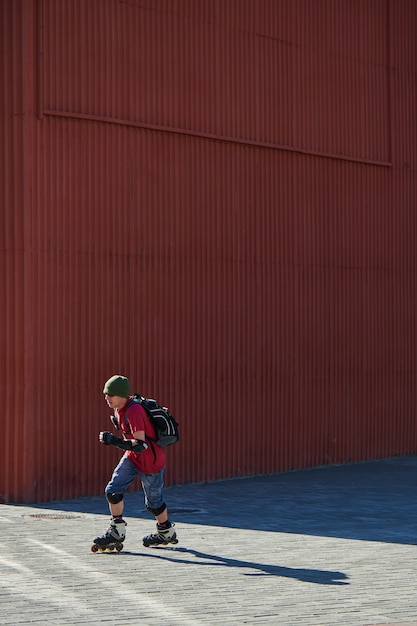 Guy paseos en patines en la acera contra la pared roja