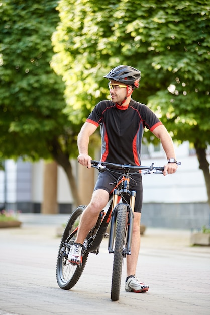 Guy professioneller Radfahrer, der nahe Fahrrad steht und interessiert und neugierig zur Seite schaut. Sportler mit Pause nach hartem Training. Konzept des gesunden Lebensstils