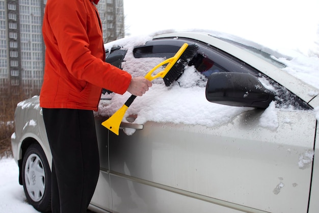 Guy reinigt den Schnee mit einer Bürste vom Auto, ein Mann kümmert sich im Winter um das Auto