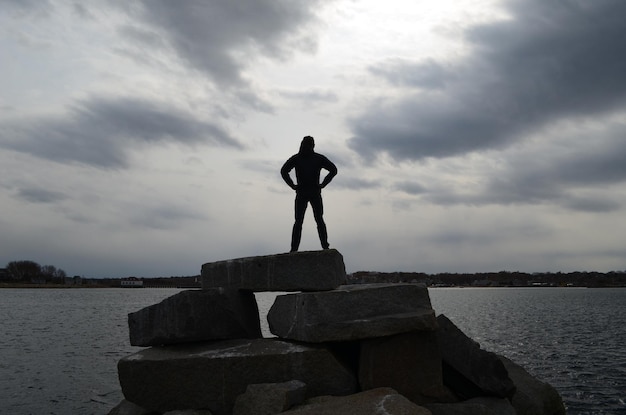 Guy silueta contra el cielo tormentoso en una pose de superhéroe en un embarcadero de roca.