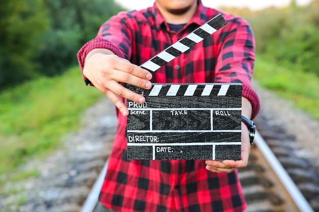 Foto guy sostiene claqueta negra en las manos. el hombre está dirigiendo y filmando una película de cine amateur. senderos ferroviarios en el fondo, concepto de viaje.