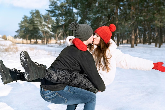 Guy sostiene a su amada en sus brazos y la besa Pareja joven enamorada camina en el bosque de invierno y tontea