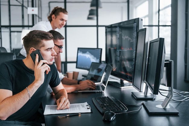 Guy telefoniert Das Team von Börsenmaklern arbeitet in einem modernen Büro mit vielen Bildschirmen