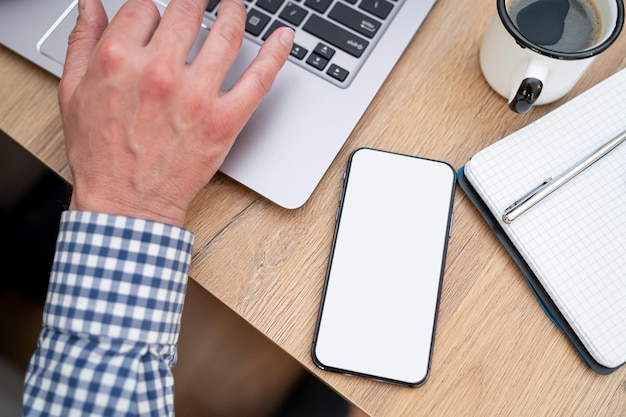 Guy verwendet einen Laptop. Männlicher Freiberufler, der sich über ein Netbook mit dem Internet verbindet. Er überprüft das Postfach am Morgen. Seien Sie jederzeit online. Bürogeräte wie Notizstift und Handy in der Ansicht von oben