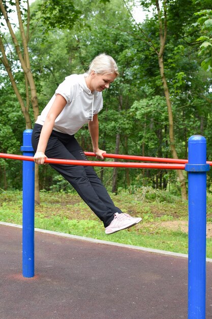 Gymnastik außerhalb der Frau im Park ist mit Gymnastikmädchen am Reck beschäftigt