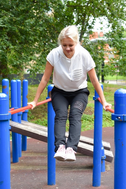 Gymnastik außerhalb der Frau im Park ist mit Gymnastikmädchen am Reck beschäftigt