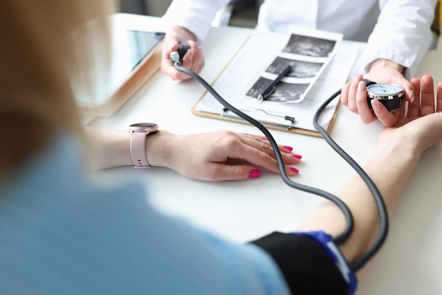 Gynäkologe Arzt, der den Blutdruck einer jungen schwangeren Frau in der Kliniknahaufnahme misst