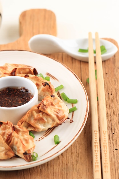 Gyoza asiáticos Potstickers com molhos servidos em placa de estilo japonês de cerâmica marrom com pauzinhos e cebolinha sobre fundo branco de madeira. Fritadeira para cozinhar sem óleo.