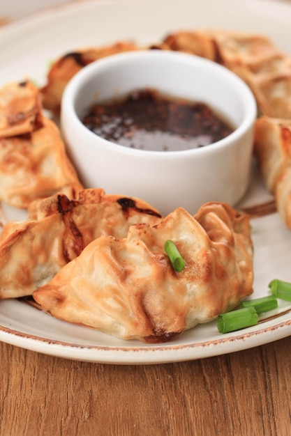 Gyoza asiáticos Potstickers com molhos servidos em placa de estilo japonês de cerâmica marrom com pauzinhos e cebolinha sobre fundo branco de madeira. Fritadeira para cozinhar sem óleo.