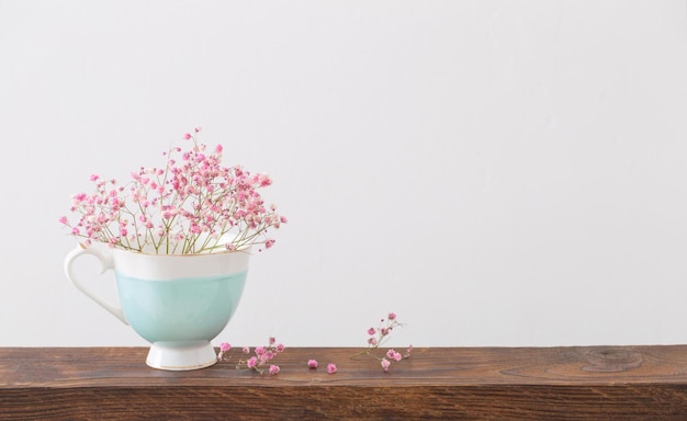 Gypsophila rosa no copo azul na prateleira de madeira no fundo branco