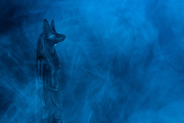 Ägyptische Statue des Todesgottes Anubis aus schwarzem Stein in blauem Nebel auf schwarzem Hintergrund