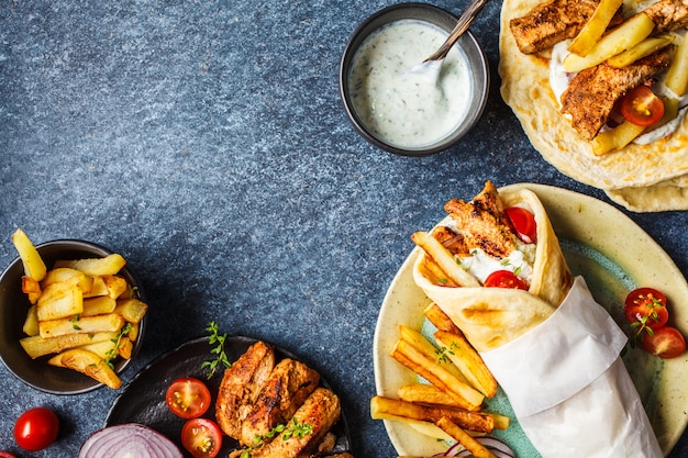 Gyros souvlaki envuelve en pan de pita con pollo, papas y salsa tzatziki, ingredientes de fondo.