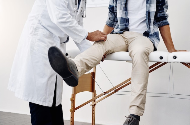 Há alguma dor aqui Foto recortada de um médico irreconhecível fazendo um check-up em um jovem paciente que está sentado na cama de um médico