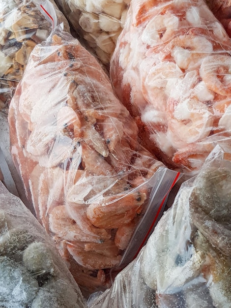 Há muitos sacos plásticos grandes com camarão cru congelado e cozido no balcão do mercado de peixe