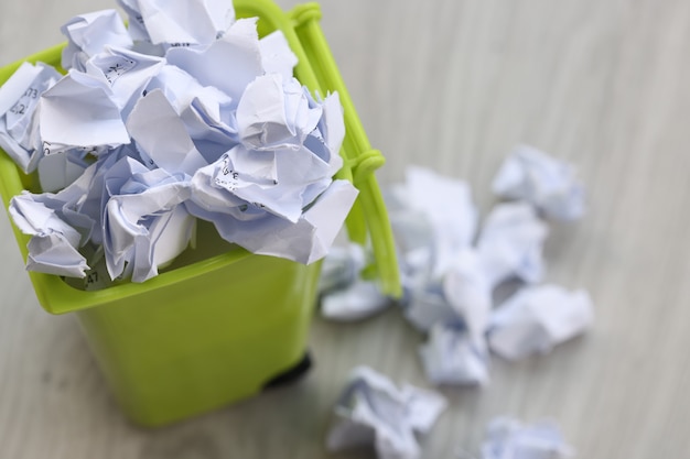 Há pedaços de papel amassados na lata de lixo verde reciclando o conceito de papel usado