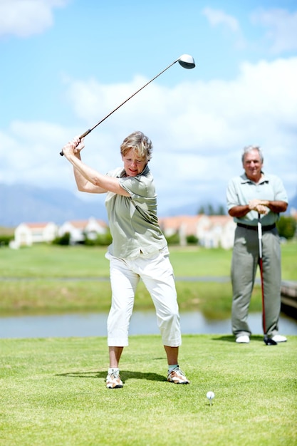 Ha perfeccionado su swing a lo largo de los años. Imagen de una mujer madura en pleno swing durante un partido de golf con su marido.