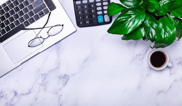 Há um laptop óculos uma calculadora uma xícara de café e uma planta verde na mesa de luz de trabalho modelo closeup do local de trabalho conceito de negócios copiar espaço