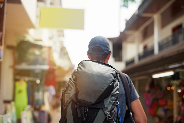 Há um mundo inteiro lá fora Foto retrovisor de um jovem turista usando uma mochila andando por uma rua da cidade