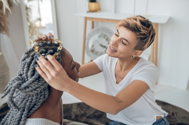 Haar Styling. Kurzhaariges Mädchen, das ihrer Freundin Haare macht und involviert aussieht