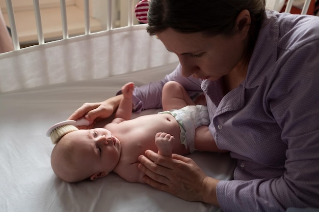 Haarbürste und Babypflege. Mutter, die kaukasisches neugeborenes Haar kämmt