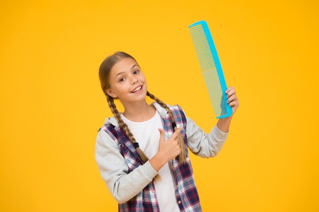 Haare kämmen Fröhliches kleines Kind mit Haarbürste Friseurschule Kurse für Friseur Bildungskurse Tangled Hair Friseurbedarf Mädchen halten enormen Kamm Friseursalon