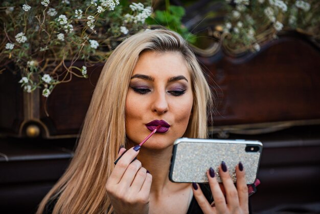 Haare wie feuer. blonde schönheit benutzt telefon als spiegel. make-up-tutorial modeblog. sexy dame legte lippenstift auf die lippen. kosmetik und make-up. folge meiner mode. bereiten sie sich auf das treffen vor. sieht immer gut aus.