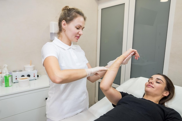 Haarentfernungsverfahren mit Zuckerpaste Shugaring Der Kosmetiker trägt Zuckerpaste auf die Hand einer jungen Frau auf