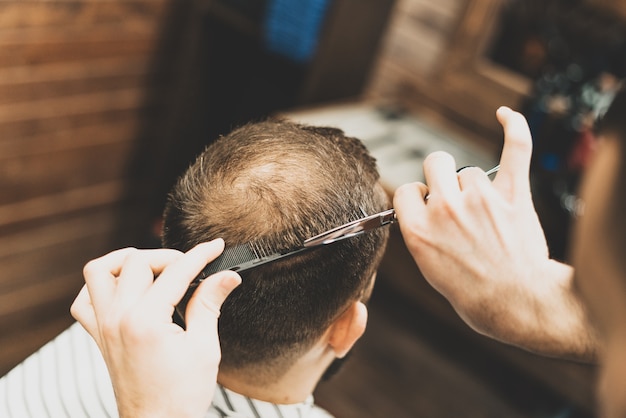 Haarschnitt beim Friseur. Barber schneidet dem Kunden die Haare auf den Kopf. Der Prozess der Erstellung von Frisuren für Männer. Ein Mann in einem Friseurladen. Der nahe Plan. Gerätestylist. Selektiver Fokus