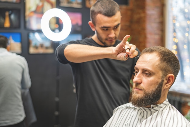 Haarschnitt beim Friseur. Barber schneidet dem Kunden die Haare auf den Kopf. Der Prozess der Erstellung von Frisuren für Männer. Ein Mann in einem Friseurladen. Der nahe Plan. Gerätestylist. Selektiver Fokus