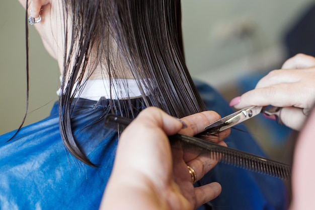 Haarschnitt in einem Schönheitssalon Die Hände eines Friseursalons schneiden brünette Haare aus der Nähe