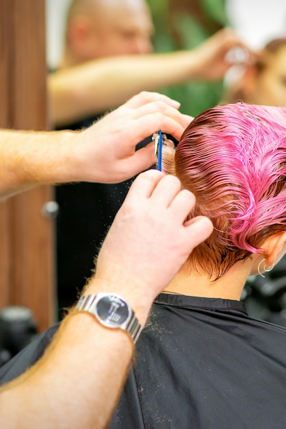 Haarschnitt von gefärbten kurzen rosafarbenen nassen Haaren einer jungen kaukasischen Frau von einem männlichen Friseur in einem Friseursalon