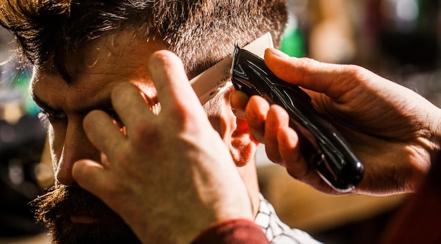 Haarschnittkonzept Mann besucht Friseur im Friseursalon Friseur arbeitet mit Haarschneidemaschine Hipster-Kunde bekommt Haarschnitt Hände des Friseurs mit Haarschneidemaschine aus nächster Nähe