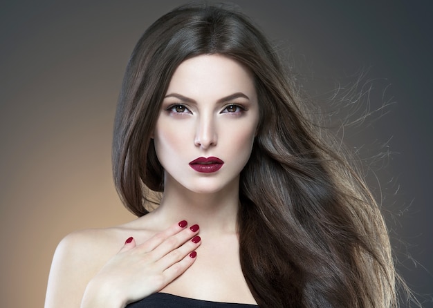 Haarschönheitsfrau lange bruette glatte schöne Manikürenägel modellieren rotes Lippenstiftbraunes Hintergrundabend-Make-upporträt. Studioaufnahme.