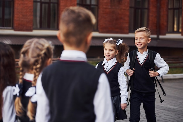 Habe eine besprechung. gruppe von kindern in schuluniform, die sich im freien in der nähe des bildungsgebäudes befindet.