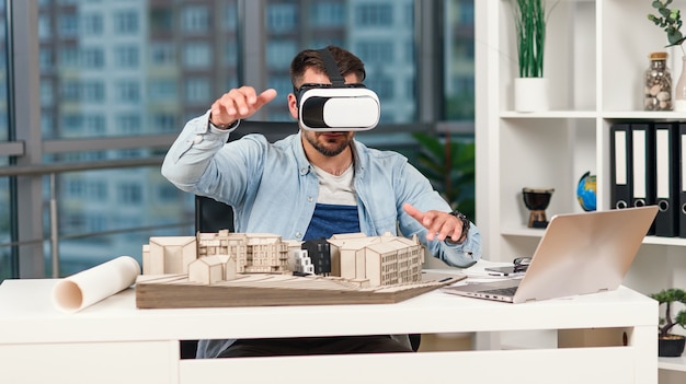 Hábil arquitecto masculino revisando proyecto arquitectónico con gafas vr en la oficina moderna.