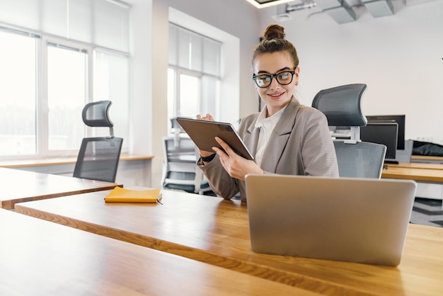 Una hábil mujer de negocios consulta su tableta digital con interés una computadora portátil abierta en la parte delantera