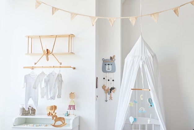 Foto habitación infantil interior blanca de estilo escandinavo, dormitorio, guardería. cuna con dosel. estantes y juguetes de madera. estante de madera en forma de avión.