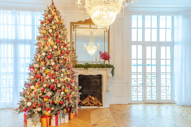 Habitación interior con decoración navideña clásica, árbol de año nuevo con adornos rojos y dorados. Apartamento de diseño de interiores de estilo clásico blanco moderno con chimenea y árbol de Navidad. Nochebuena en casa.