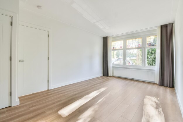 Una habitación vacía y luminosa con grandes ventanales y suelo de madera.