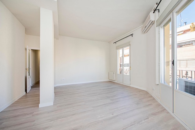 Habitación vacía recién pintada con pisos de madera, miradores de piso a techo y unidad de aire acondicionado